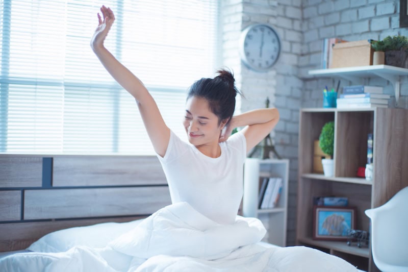 Woman sitting up in bed stretching.